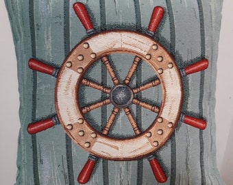 May include: A decorative cushion with a blue and green striped background featuring a brown wooden ship's wheel with a metal centre.