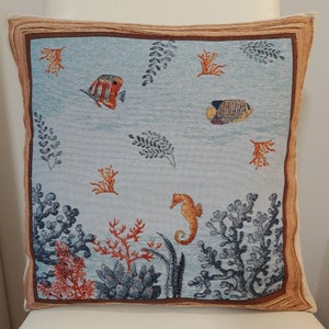 May include: A blue and white throw pillow with an embroidered design of seahorses, fish, and coral. The pillow has a brown border.
