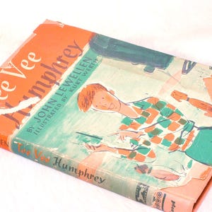 May include: Vintage hardcover book titled "Tee Vee Humphrey" by John Lewellen, illustrated by Kurt Werth. The cover features an illustration of a boy in a green and orange plaid shirt. The book has an orange spine and a worn appearance.