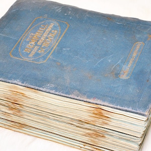 May include: A vintage book with a faded blue cover. The cover features gold lettering that reads "The Hemphill Diesel Engineering Schools." The pages are aged and show signs of wear.