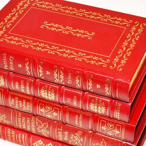 May include: A stack of red leather-bound books with gold embossed titles and decorative borders. The titles include "Patrick Henry", "The French and Indian Wars", and "The Life of Ralph Waldo Emerson". The books are stacked on top of each other.