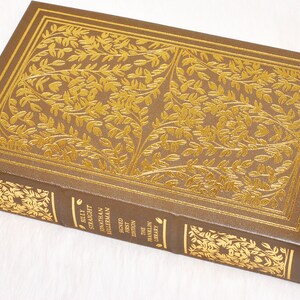 May include: A hardcover book with a brown cover and gold leaf detailing. The cover features an embossed floral design and the spine displays the title "Billy Straight" and author information. The book is a first edition from The Franklin Library.