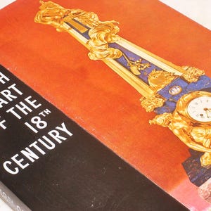 May include: A book titled "French Art of the 18th Century" with a red and black cover. The cover features a gold-colored decorative element with a clock and blue accents. The book's title is in white letters.