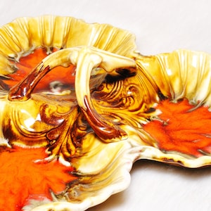 May include: A vintage ceramic serving dish with three sections and a handle. The dish features a leaf-like design with a cream-colored exterior, a vibrant orange center, and brown accents. The handle is also cream and brown.