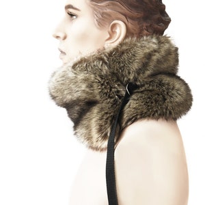 May include: A brown faux fur collar with a black adjustable strap. The collar is worn by a mannequin.