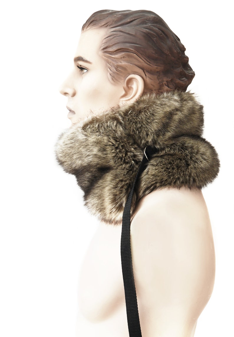 May include: A brown faux fur collar with a black adjustable strap. The collar is worn by a mannequin.