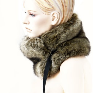 May include: A brown faux fur collar with a black strap. The collar is worn by a mannequin with blonde hair.