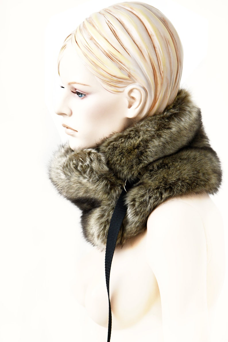 May include: A brown faux fur collar with a black strap. The collar is worn by a mannequin with blonde hair.