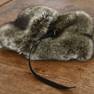 May include: A brown faux fur hat with a black strap and buckle. The hat has a long, fluffy brim and is made of soft, plush material.