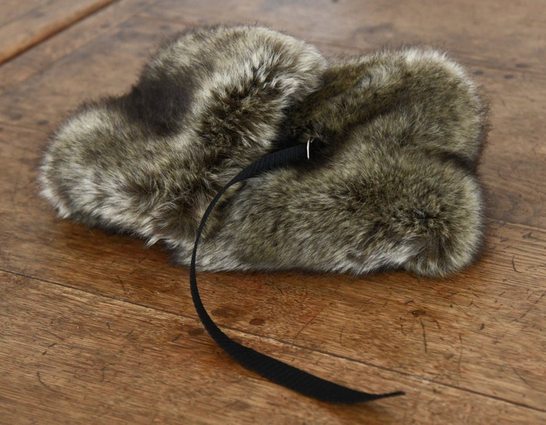 May include: A brown faux fur hat with a black strap and buckle. The hat has a long, fluffy brim and is made of soft, plush material.