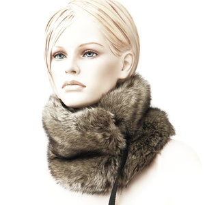 May include: A brown faux fur neck warmer with a black strap. The neck warmer is worn by a mannequin with blonde hair.