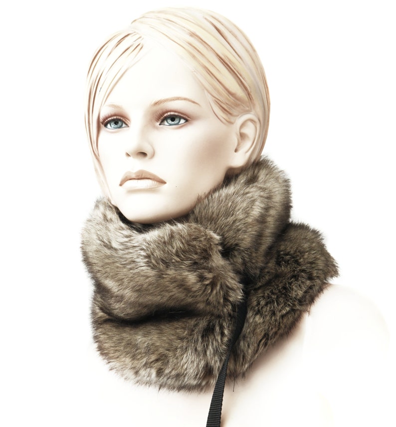 May include: A brown faux fur neck warmer with a black strap. The neck warmer is worn by a mannequin with blonde hair.