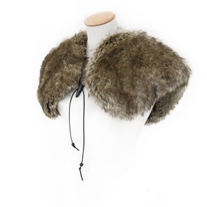 May include: A brown faux fur collar with a black leather tie closure. The collar is displayed on a white mannequin.