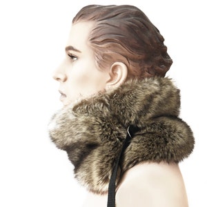 May include: A brown faux fur collar with a black adjustable strap. The collar is worn by a mannequin with brown hair.