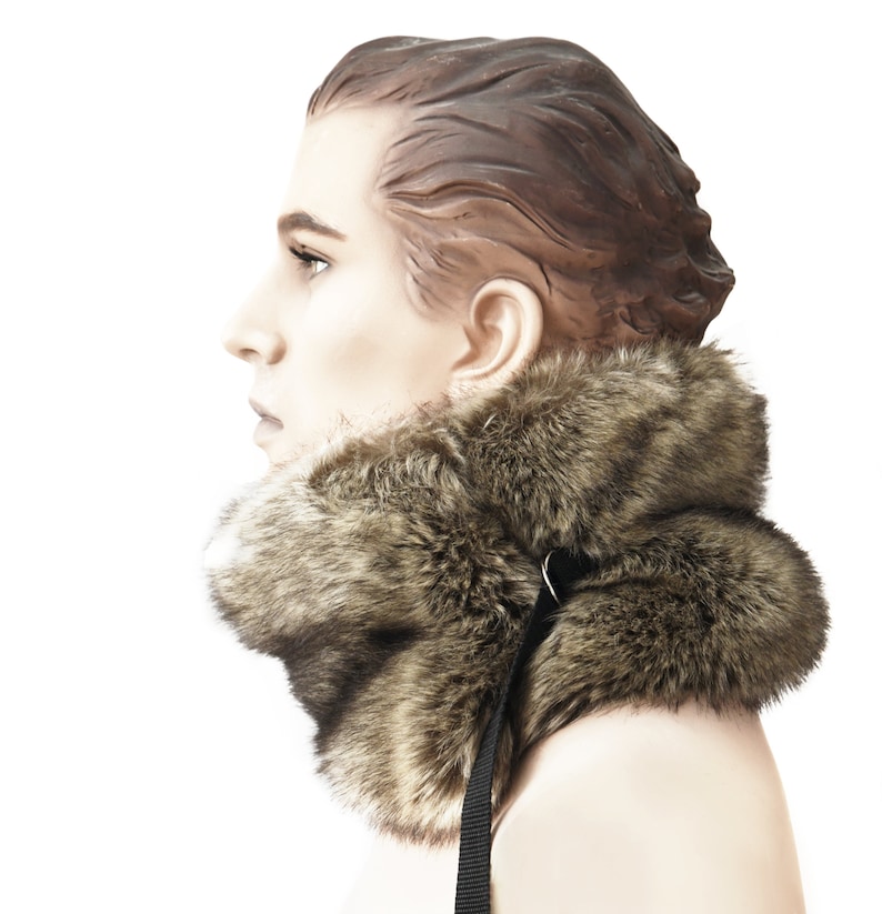 May include: A brown faux fur collar with a black adjustable strap. The collar is worn by a mannequin with brown hair.