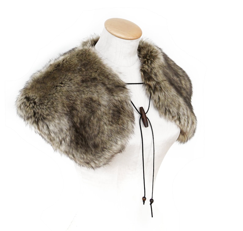 May include: A brown faux fur collar with a black leather tie and wooden beads. The collar is on a white mannequin.