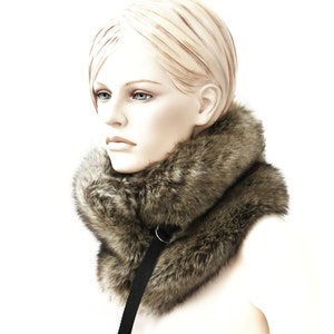 May include: A brown faux fur collar with a black strap. The collar is worn by a mannequin with blonde hair.