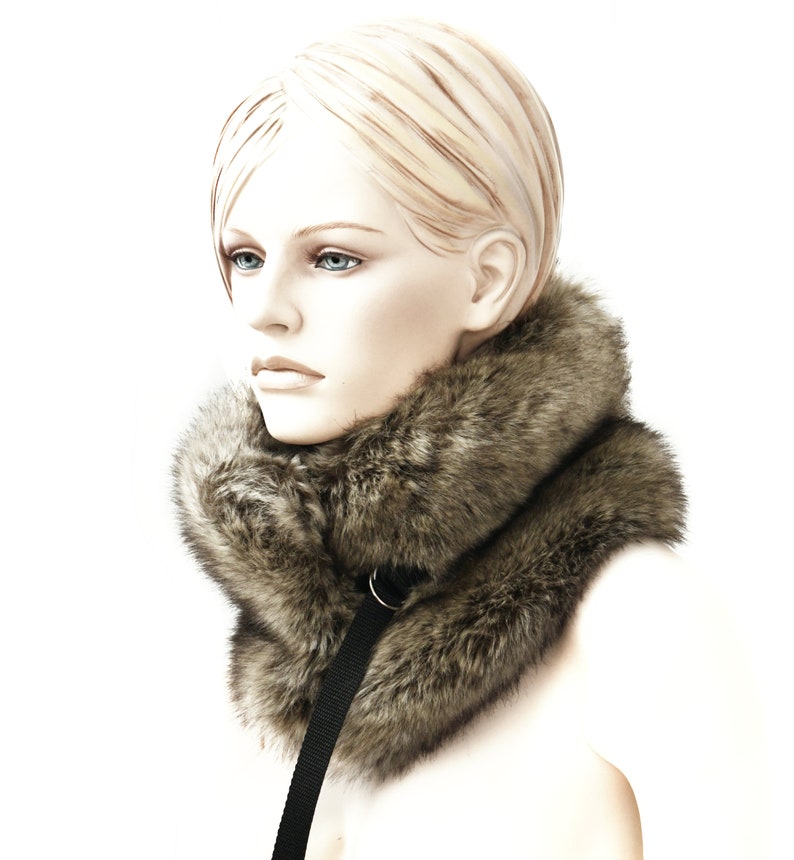 May include: A brown faux fur collar with a black strap. The collar is worn by a mannequin with blonde hair.