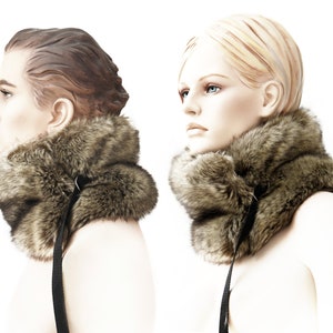 May include: A brown faux fur neck warmer with a black strap and buckle closure. The neck warmer is shown on two mannequins.