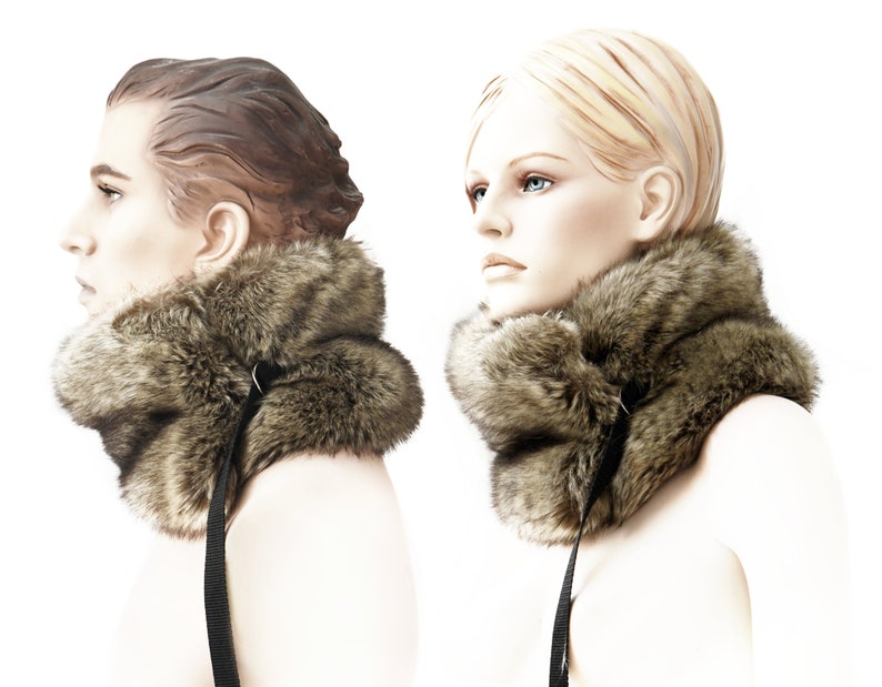 May include: A brown faux fur neck warmer with a black strap and buckle closure. The neck warmer is shown on two mannequins.