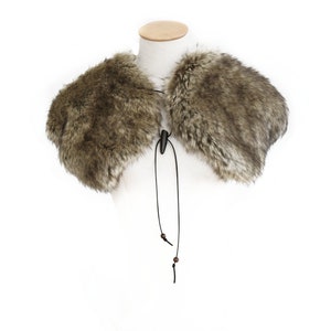 May include: A brown faux fur collar with a black leather tie and wooden beads. The collar is on a white mannequin.