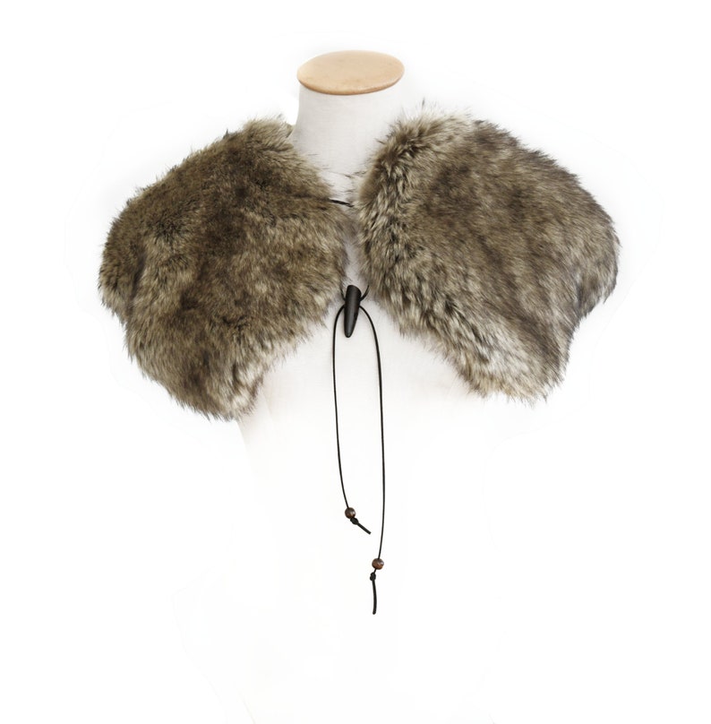 May include: A brown faux fur collar with a black leather tie and wooden beads. The collar is on a white mannequin.