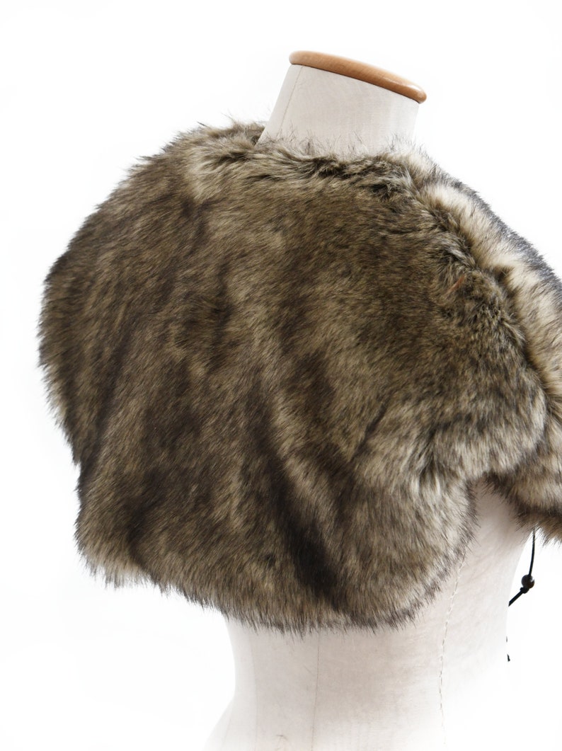 May include: A brown faux fur shawl with a short, cropped length. The shawl is made of soft, fluffy faux fur and has a simple, elegant design.