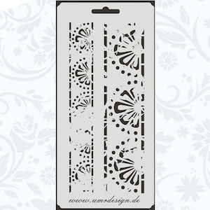 May include: A black and white stencil with a repeating pattern of stylized flowers and dots. The stencil is designed for crafting and decorating projects. The text "www.umrdesign.de" is printed at the bottom of the stencil.
