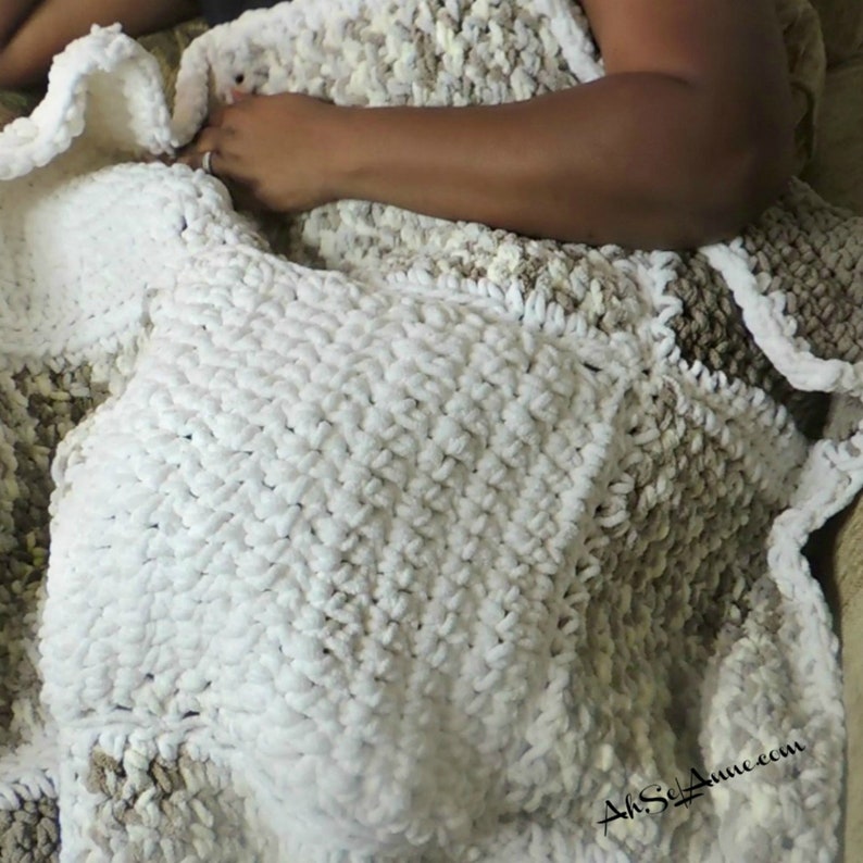 May include: A white and beige crocheted throw blanket with a textured pattern. The blanket is folded and draped over a chair.