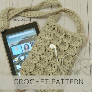 May include: A crocheted beige crossbody bag with a long strap. The bag is large enough to hold a tablet, and the image shows it holding a tablet with a screen displaying the Amazon Kindle app. The text "CROCHET PATTERN" is printed below the bag.