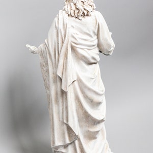 May include: White painted figurine of a person wearing a long robe with their back to the viewer. The figurine is standing on a base.