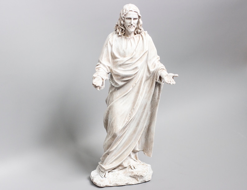 May include: White painted figurine of a man in a long robe with his arms outstretched. The figurine is standing on a base.