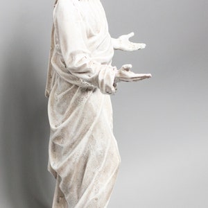 May include: White painted statue of Jesus with long hair and beard, wearing a robe, standing with arms outstretched.