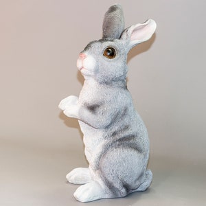 May include: A gray rabbit figurine with brown eyes, standing on its hind legs with its front paws raised. The rabbit has a white belly and a gray and white striped pattern on its back.