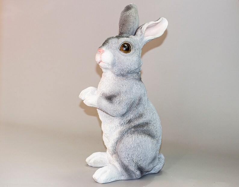 May include: A gray rabbit figurine with brown eyes, standing on its hind legs with its front paws raised. The rabbit has a white belly and a gray and white striped pattern on its back.