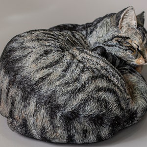 May include: A gray and black tabby cat sculpture curled up in a sleeping position.