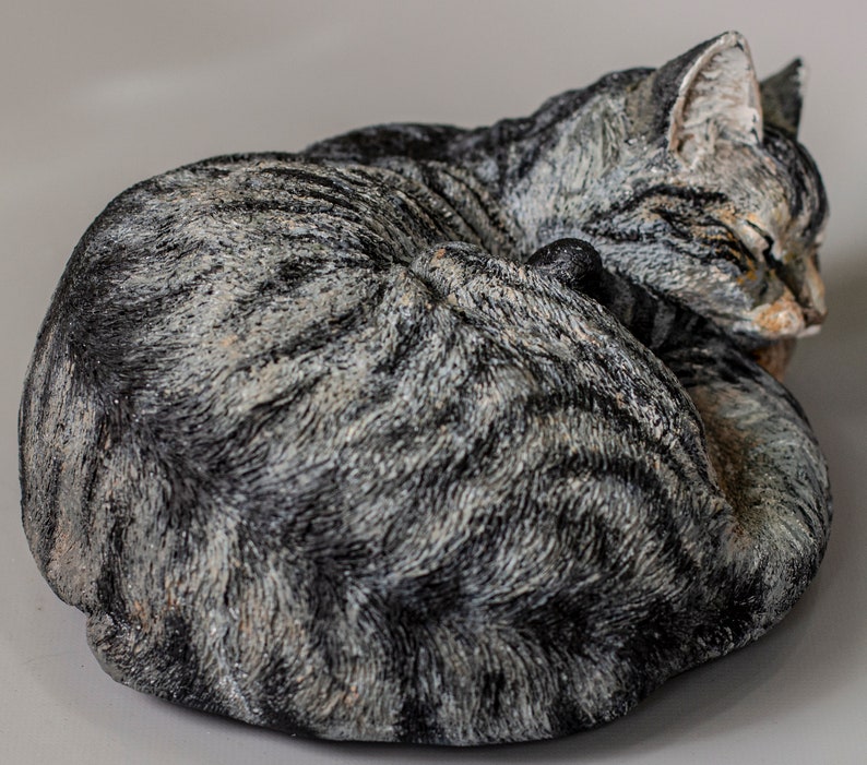May include: A gray and black tabby cat sculpture curled up in a sleeping position.