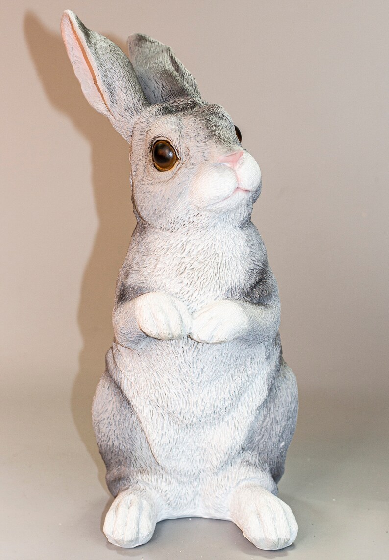 May include: A gray and white rabbit figurine with brown eyes. The rabbit is sitting upright with its paws crossed in front of it.