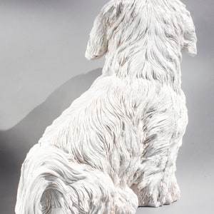 May include: White ceramic figurine of a dog sitting with its tail curled around its legs. The dog has a fluffy, textured coat and is depicted in a realistic style.