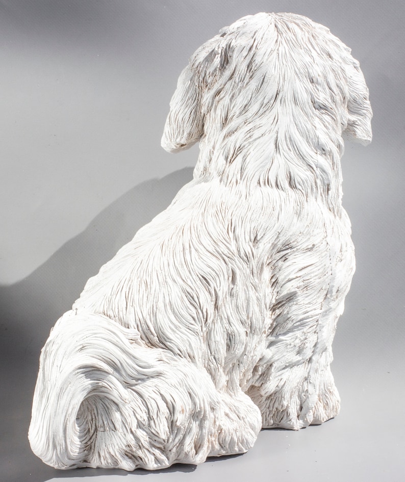 May include: White ceramic figurine of a dog sitting with its tail curled around its legs. The dog has a fluffy, textured coat and is depicted in a realistic style.