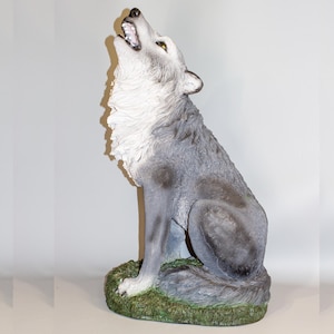 May include: A gray and white wolf statue with its mouth open, howling at the sky. The wolf is sitting on a green base with brown accents.