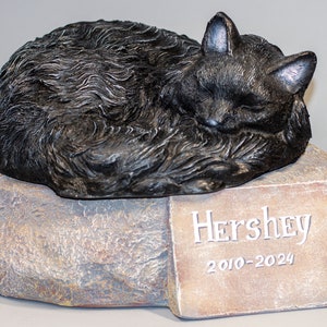 May include: Black cat figurine sleeping on a stone base with a plaque that reads "Hershey 2010-2024".