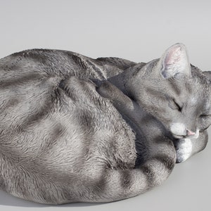 May include: A gray and white sleeping cat figurine. The cat is curled up in a ball with its eyes closed. The figurine is made of a realistic material and is perfect for adding a touch of whimsy to any home.