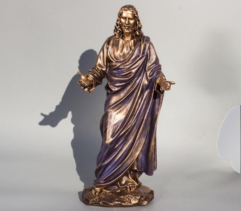 May include: A gold-toned statue of Jesus Christ with a purple robe and outstretched arms. The statue is standing on a brown base.