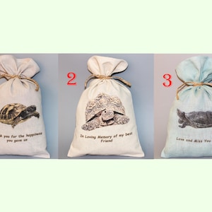 Puede incluir: Tres bolsas de tela blancas y azules con diferentes diseños de tortugas y texto. La primera bolsa dice "Gracias por la felicidad que nos diste". La segunda bolsa dice "En memoria cariñosa de mi mejor amigo". La tercera bolsa dice "Te quiero y te extraño para siempre".