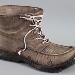 Peut inclure: Une botte en cuir marron avec des lacets blancs et un aspect usé. La botte a une semelle épaisse et une pointe arrondie.