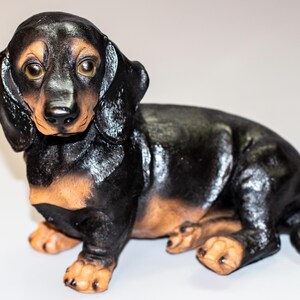 Könnte beinhalten: Schwarze und braune Dackelfigur. Die Figur sitzt mit leicht geneigtem Kopf. Der Dackel hat eine schwarze Nase und braune Augen.