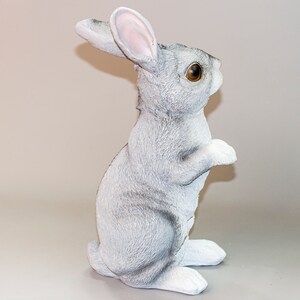 May include: A gray and white rabbit figurine standing on its hind legs with its front paws raised. The rabbit has brown eyes and a fluffy tail.