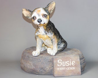 May include: A ceramic figurine of a small, brown, black, and white chihuahua dog sitting on a gray rock. The dog has a name tag that reads "Susie 11/12/07 - 2/24/24".