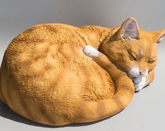 May include: A ceramic sculpture of an orange tabby cat curled up asleep. The cat has white markings on its chest and paws.
